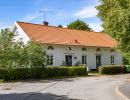En bild på ett vackert vitmålat gammalt hus omgivet av gröna buskar.