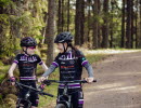 Two girls on a mountain bike in the woods, black club clothes. forest path behind them.