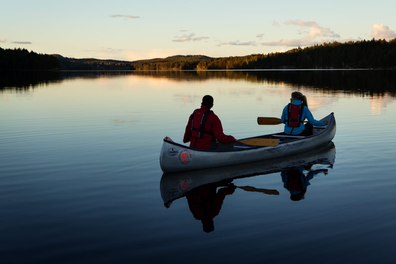 Par i kanot på spegelblank sjö paddlar genom skogslandskap