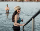 The woman is standing with a winter hat on and going down a ladder into the water. Lots of houses can be seen in the background